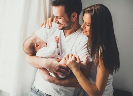Ein Elternpaar steht mit ihrem Baby am Fenster.