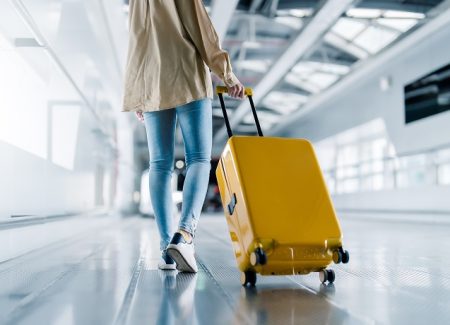 Eine Frau zieht auf einem Flughafen einen gelben Koffer hinter sich