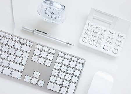 Ein Taschenrechner, ein Wecker, ein Kugelschreiber und eine Tastatur liegen auf einer Unterlage