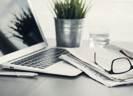 Eine Zeitschrift und eine Brille liegen neben einem aufgeklappten Laptop