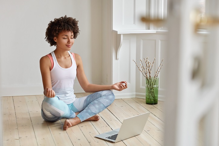 Eine Frau sitzt in einer Yogastellung auf dem Boden und nimmt an einem Online-Kurs Yoga teil