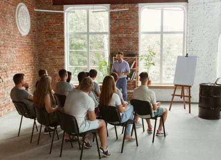Eine Gruppe von jungen Menschen sitzt in einem Raum und hört dem Seminarleiter zu