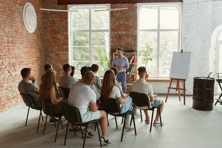 Eine Gruppe von jungen Menschen sitzt in einem Raum und hört dem Seminarleiter zu