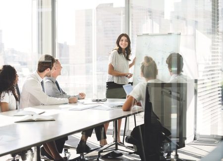 Eine Frau präsentiert mit Hilfe eines Whiteboards in einem Besprechungsraum vor einem Team.