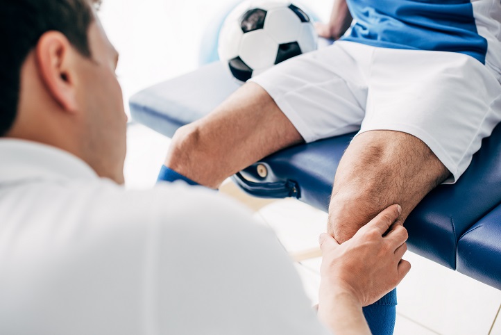 Ein Arzt untersucht das Knie eines Fußballspielers, der auf einer Liege sitzt