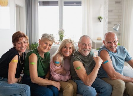 Eine Gruppe von Senioren zeigt ihre Oberarme mit bunten Pflastern nach einer Impfung