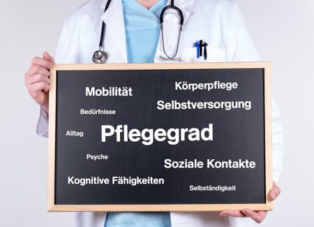 Ein Arzt hält eine Tafel mit Begriffen wie Pflegegrad, Körperpflege etc. vor sich