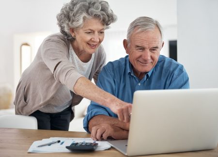 Ein älteres Paar schaut auf einem Laptop, welches auf dem Tisch liegt.