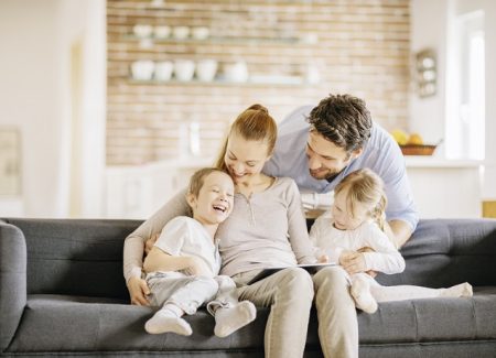Ein junges Elternpaar sitzt mit zwei Kindern im Wohnzimmer auf einem Sofa