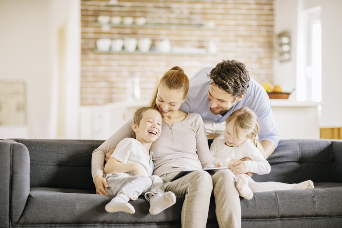 Ein junges Elternpaar sitzt mit zwei Kindern im Wohnzimmer auf einem Sofa