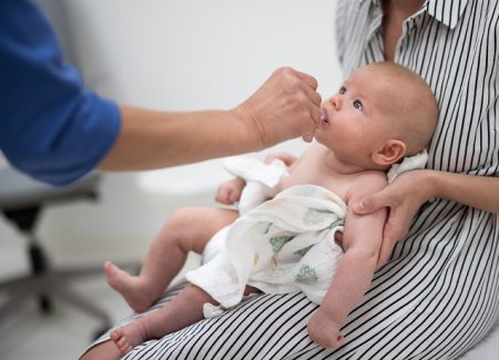 Ein Baby liegt auf dem Schoss der Mutter und bekommt Arzneimittel verabreicht