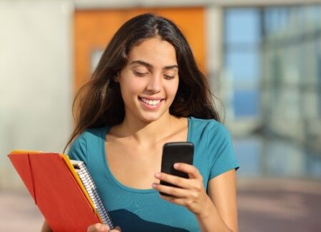 Eine Frau schaut lächelnd auf das Display ihres Smartphones.