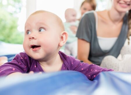 Ein Baby mit der Mutter im Hintergrund liegt auf einer blauen Matte