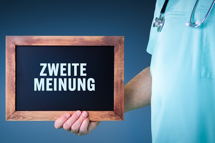 Ein Mann hält ein Schild in der Hand. Auf dem Schild steht Zweite Meinung