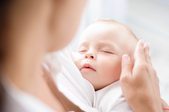Eine Nahaufnahme eines friedlich schlafenden Babys in den Armen eines Erwachsenen, der sanft den Kopf des Babys berührt.