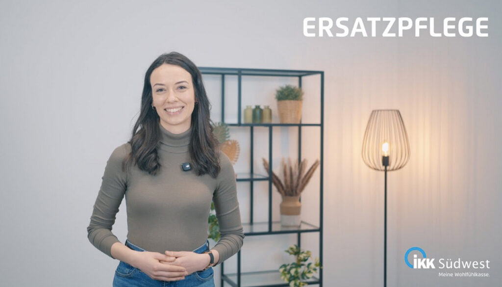 Eine Frau steht lächelnd in einem modernen Raum mit Regalen, einer Lampe und Pflanzen. Oben steht das Wort ERSATZPFLEGE, unten rechts ist das Logo der IKK Südwest zu sehen.