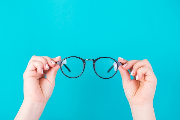 Ein Paar Hände hält eine runde schwarze Brille vor einem hellblauen Hintergrund.