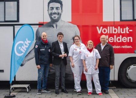 Fünf Personen stehen lächelnd vor einem weißen Bus mit einem großen Rotkreuz-Logo und der Aufschrift Vollblut-Helden.