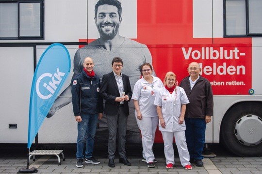 Fünf Personen stehen lächelnd vor einem weißen Bus mit einem großen Rotkreuz-Logo und der Aufschrift Vollblut-Helden.