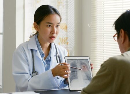 Ein Arzt im weißen Kittel zeigt einem Patienten ein Röntgenbild auf einem Tablet und bespricht die Ergebnisse in einer hellen Arztpraxis.