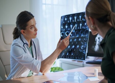 Ein Arzt in einem weißen Kittel zeigt auf ein Hirnscanbild auf einem Leuchtkasten und erklärt einem Patienten, der ihm gegenüber sitzt, die Ergebnisse in einer Arztpraxis.