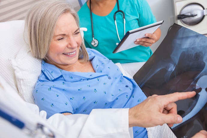 Eine Frau liegt im Krankenhausbett und ein Arzt zeigt ihr ein R&ouml;ntgenbild.