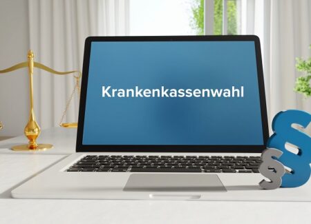 Auf dem Bildschirm eines Laptops wird das Wort "Krankenkassenwahl" angezeigt. Neben dem Laptop befindet sich ein blaues Paragraphen-Symbol.